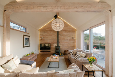 Scandinavian living room in Cornwall with white walls, medium hardwood floors, a wood stove and brown floor.