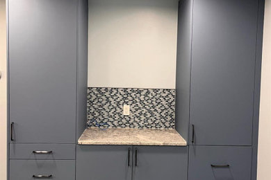 Dedicated laundry room - mid-sized modern l-shaped dedicated laundry room idea in Bridgeport with flat-panel cabinets, blue cabinets, granite countertops, black backsplash, mosaic tile backsplash, gray walls and yellow countertops