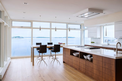 Photo of a contemporary eat-in kitchen in Boston with an undermount sink, flat-panel cabinets, white cabinets, white splashback, light hardwood floors, with island and glass sheet splashback.