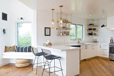 Inspiration for a mid-sized contemporary u-shaped medium tone wood floor and brown floor open concept kitchen remodel in Toronto with a double-bowl sink, flat-panel cabinets, white cabinets, white backsplash, wood backsplash, stainless steel appliances, a peninsula, beige countertops and solid surface countertops