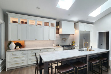 Mid-sized transitional galley medium tone wood floor, brown floor and vaulted ceiling kitchen photo in Charlotte with an undermount sink, shaker cabinets, white cabinets, quartzite countertops, gray backsplash, stainless steel appliances, an island, gray countertops and stone slab backsplash