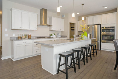 Photo of a large transitional eat-in kitchen in Minneapolis with flat-panel cabinets, white cabinets, quartz benchtops, stainless steel appliances, medium hardwood floors, with island and a double-bowl sink.