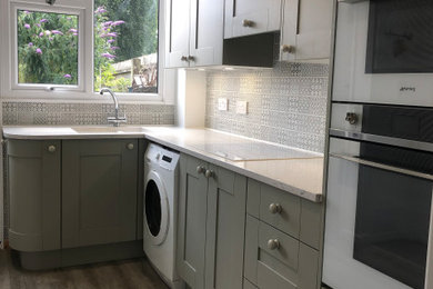 This is an example of a medium sized classic l-shaped kitchen/diner in Other with an integrated sink, shaker cabinets, green cabinets, quartz worktops, blue splashback, ceramic splashback, white appliances, vinyl flooring, no island, brown floors and white worktops.
