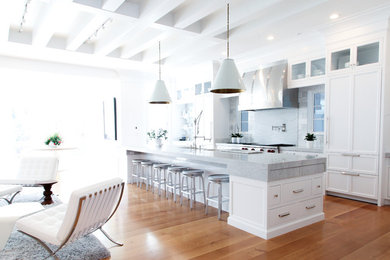 Inspiration for a large transitional l-shaped medium tone wood floor open concept kitchen remodel in Salt Lake City with a farmhouse sink, white cabinets, marble countertops, stone tile backsplash, paneled appliances and an island