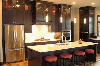 Large transitional l-shaped medium tone wood floor eat-in kitchen photo in Milwaukee with an undermount sink, recessed-panel cabinets, dark wood cabinets, quartz countertops, white backsplash, ceramic backsplash, stainless steel appliances and an island
