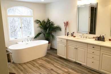 Freestanding bathtub - large contemporary master medium tone wood floor and brown floor freestanding bathtub idea in Other with raised-panel cabinets, gray cabinets, a two-piece toilet, white walls, an integrated sink and granite countertops