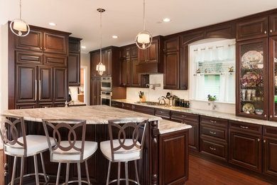 Example of a large trendy l-shaped medium tone wood floor and brown floor eat-in kitchen design in San Francisco with a drop-in sink, raised-panel cabinets, dark wood cabinets, laminate countertops, white backsplash, ceramic backsplash, stainless steel appliances and an island
