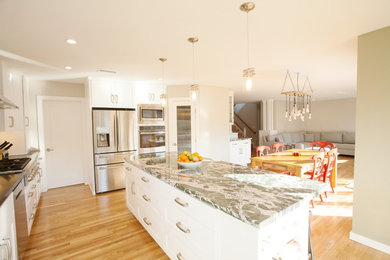 This is an example of a mid-sized beach style l-shaped open plan kitchen in San Diego with an undermount sink, recessed-panel cabinets, white cabinets, quartz benchtops, white splashback, glass tile splashback, stainless steel appliances, medium hardwood floors, with island and brown floor.