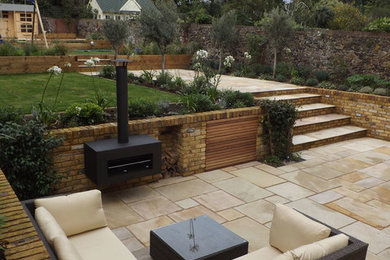 Large mediterranean backyard full sun garden in Kent with natural stone pavers for summer.