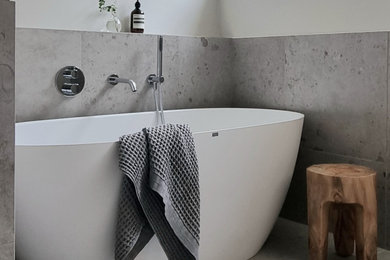 Inredning av ett minimalistiskt stort grå grått bastu, med släta luckor, beige skåp, ett fristående badkar, en dusch/badkar-kombination, grå kakel, stenkakel, grå väggar, kalkstensgolv, ett undermonterad handfat, bänkskiva i kalksten, grått golv och dusch med skjutdörr