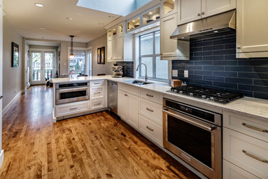 Mid-sized transitional l-shaped eat-in kitchen in Vancouver with shaker cabinets, white cabinets, marble benchtops, black splashback, subway tile splashback, stainless steel appliances, medium hardwood floors, a peninsula, brown floor, an undermount sink and white benchtop.
