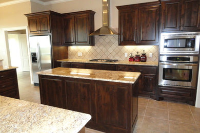 Inspiration for a large transitional u-shaped ceramic tile enclosed kitchen remodel in Austin with raised-panel cabinets, dark wood cabinets, granite countertops, beige backsplash, stone tile backsplash, stainless steel appliances and an island