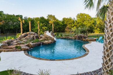 Example of a large island style backyard stone and custom-shaped water slide design in Dallas