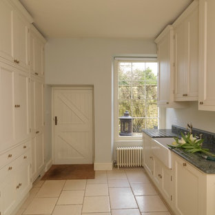 ロンドンの中サイズのトラディショナルスタイルのおしゃれな家事室 (エプロンフロントシンク、落し込みパネル扉のキャビネット、白いキャビネット、御影石カウンター、白い壁、ライムストーンの床、目隠し付き洗濯機・乾燥機) の写真