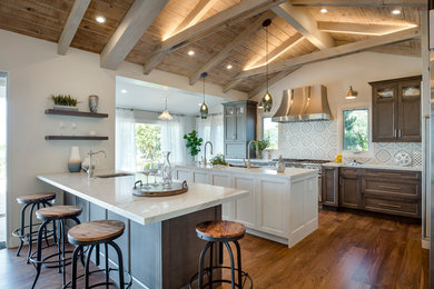 Large country u-shaped medium tone wood floor, brown floor, exposed beam, vaulted ceiling and wood ceiling kitchen photo in Los Angeles with quartz countertops, multicolored backsplash, stainless steel appliances, two islands, dark wood cabinets, cement tile backsplash, an undermount sink, white countertops and recessed-panel cabinets