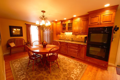 Eat-in kitchen - mid-sized traditional single-wall light wood floor eat-in kitchen idea in Other with an undermount sink, raised-panel cabinets, medium tone wood cabinets, granite countertops, brown backsplash, ceramic backsplash and black appliances
