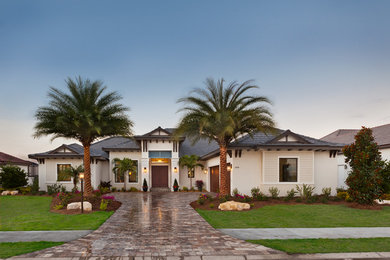 This is an example of an expansive beach style one-storey stucco beige house exterior in Tampa with a hip roof and a shingle roof.