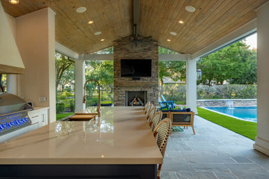 ヒューストンにあるラグジュアリーな広いおしゃれな裏庭のテラス (屋外暖炉、天然石敷き、張り出し屋根) の写真