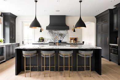 Large transitional u-shaped eat-in kitchen in Vancouver with an undermount sink, recessed-panel cabinets, black cabinets, marble benchtops, white splashback, granite splashback, black appliances, light hardwood floors, with island, brown floor and white benchtop.