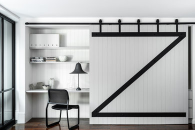 Photo of an industrial study room in Sydney with white walls, dark hardwood floors, a built-in desk, brown floor and panelled walls.