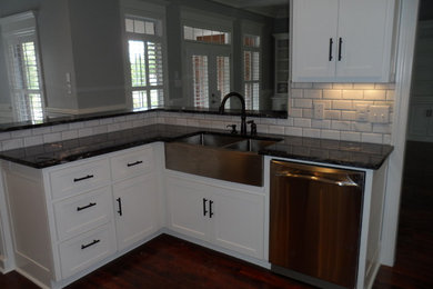 This is an example of a traditional l-shaped eat-in kitchen in Other with a double-bowl sink, shaker cabinets, white cabinets, marble benchtops, white splashback, subway tile splashback, stainless steel appliances, dark hardwood floors and a peninsula.