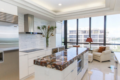 Example of a mid-sized minimalist galley beige floor enclosed kitchen design in Tampa with an undermount sink, flat-panel cabinets, white cabinets, solid surface countertops, white backsplash, marble backsplash, stainless steel appliances, an island and white countertops