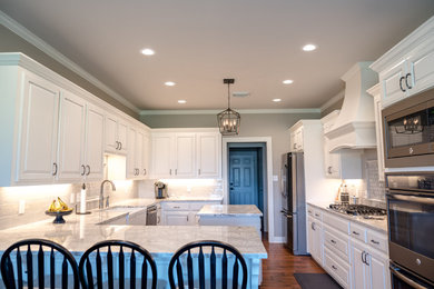Inspiration for a large transitional u-shaped medium tone wood floor and brown floor enclosed kitchen remodel in New Orleans with a farmhouse sink, raised-panel cabinets, white cabinets, quartz countertops, gray backsplash, marble backsplash, stainless steel appliances, an island and gray countertops