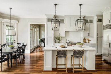 Ejemplo de cocina comedor clásica renovada grande con fregadero sobremueble, armarios estilo shaker, puertas de armario grises, encimera de cuarzo compacto, salpicadero blanco, salpicadero de azulejos de porcelana, electrodomésticos de acero inoxidable, suelo de madera en tonos medios, una isla y encimeras blancas