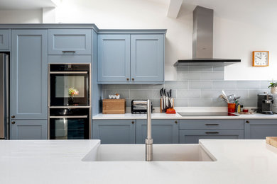 Inspiration for a large modern galley kitchen/diner in Other with an integrated sink, shaker cabinets, blue cabinets, engineered stone countertops, blue splashback, ceramic splashback, stainless steel appliances, medium hardwood flooring, a breakfast bar, multi-coloured floors, white worktops and a vaulted ceiling.