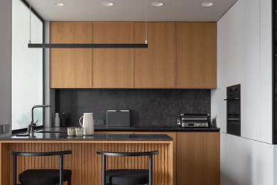 Kitchen - contemporary u-shaped gray floor kitchen idea in Moscow with flat-panel cabinets, light wood cabinets, black backsplash, black appliances, a peninsula and black countertops