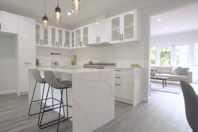 Large contemporary l-shaped eat-in kitchen in Melbourne with a double-bowl sink, glass-front cabinets, white cabinets, quartz benchtops, white splashback, subway tile splashback, stainless steel appliances, with island and grey floor.