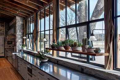 Mountain style galley medium tone wood floor kitchen photo in Austin with a farmhouse sink, gray cabinets, stainless steel appliances and an island
