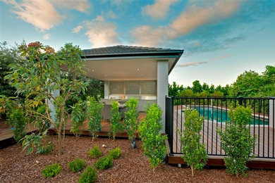 This is an example of a mid-sized modern backyard custom-shaped lap pool in Brisbane with a pool house and decking.