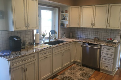 Mid-sized elegant u-shaped laminate floor and brown floor enclosed kitchen photo in Denver with an undermount sink, recessed-panel cabinets, white cabinets, granite countertops, white backsplash, ceramic backsplash, stainless steel appliances, no island and brown countertops