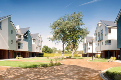 This is an example of an expansive and multi-coloured coastal front detached house in Kent with three floors, wood cladding, a pitched roof, a shingle roof, a grey roof and board and batten cladding.