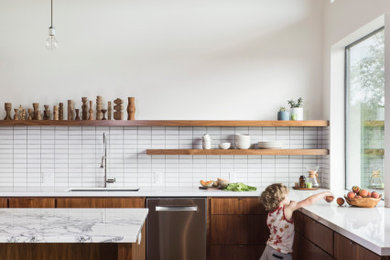 1960s l-shaped concrete floor and gray floor kitchen photo in Austin with flat-panel cabinets, medium tone wood cabinets, an island, an undermount sink, white backsplash, stainless steel appliances and white countertops