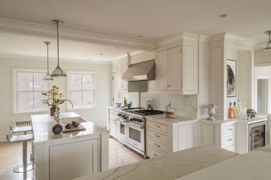 Example of a large classic l-shaped medium tone wood floor and brown floor kitchen design in New York with a farmhouse sink, beaded inset cabinets, white cabinets, marble countertops, white backsplash, marble backsplash, stainless steel appliances, an island and white countertops