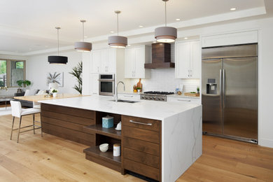 Inspiration for a mid-sized transitional galley kitchen in Calgary with an undermount sink, shaker cabinets, white cabinets, quartz benchtops, white splashback, subway tile splashback, stainless steel appliances, light hardwood floors, with island, brown floor and white benchtop.