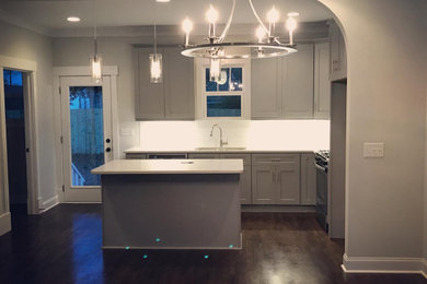 Kitchen pantry - mid-sized modern l-shaped dark wood floor, brown floor and vaulted ceiling kitchen pantry idea in Charlotte with a single-bowl sink, shaker cabinets, white cabinets, solid surface countertops, white backsplash, stainless steel appliances, an island and white countertops