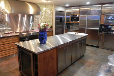 Photo of a mid-sized modern l-shaped kitchen in Dallas with flat-panel cabinets, stainless steel cabinets, stainless steel benchtops, glass sheet splashback, stainless steel appliances, slate floors, with island and brown floor.