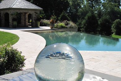 This is an example of a large traditional backyard custom-shaped infinity pool in Philadelphia with a water feature and natural stone pavers.