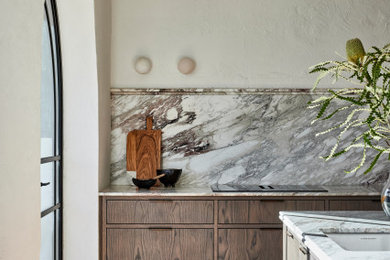This is an example of a large transitional galley eat-in kitchen in Sydney with a single-bowl sink, flat-panel cabinets, dark wood cabinets, marble benchtops, multi-coloured splashback, marble splashback, black appliances, light hardwood floors, with island, brown floor, multi-coloured benchtop and exposed beam.