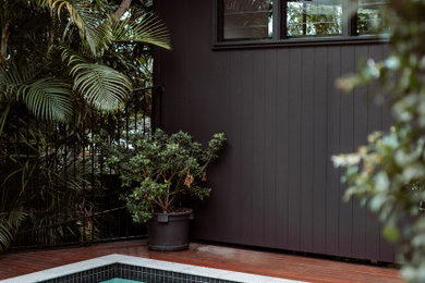 Inspiration for a mid-sized modern two-storey black house exterior in Brisbane with wood siding, a flat roof, a metal roof, a black roof and board and batten siding.