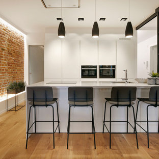 Ejemplo de cocina de galera, actual, de tamaño medio, con fregadero bajoencimera, armarios con paneles lisos, puertas de armario blancas, electrodomésticos con paneles, una isla, suelo marrón y encimeras blancas