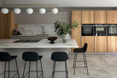 Photo of a large modern grey and black single-wall kitchen/diner in London with an integrated sink, flat-panel cabinets, grey cabinets, composite countertops, ceramic splashback, black appliances, cement flooring, an island, grey floors, a drop ceiling and feature lighting.