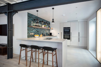 Design ideas for a small contemporary cream and black kitchen/diner in London with a built-in sink, all styles of cabinet, white cabinets, quartz worktops, blue splashback, metro tiled splashback, stainless steel appliances, light hardwood flooring, a breakfast bar and white worktops.