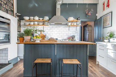 Trendy dark wood floor and brown floor kitchen photo in Sussex with white cabinets, wood countertops, white backsplash, subway tile backsplash, an island and beige countertops