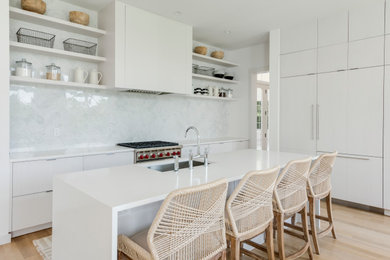Design ideas for a contemporary l-shaped kitchen in Miami with an undermount sink, flat-panel cabinets, white cabinets, white splashback, stainless steel appliances, light hardwood floors, with island, beige floor and white benchtop.