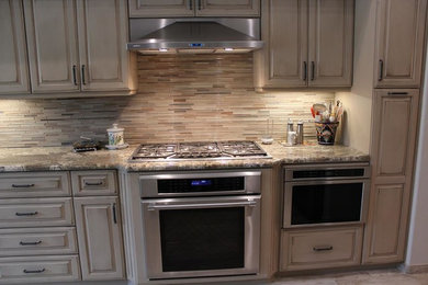 Large elegant single-wall light wood floor and beige floor enclosed kitchen photo in Phoenix with raised-panel cabinets, beige cabinets, granite countertops, beige backsplash, matchstick tile backsplash, stainless steel appliances and an island