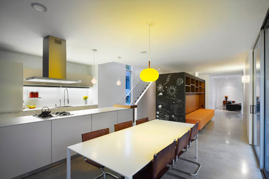 Mid-sized minimalist galley concrete floor and gray floor eat-in kitchen photo in Toronto with an undermount sink, flat-panel cabinets, white cabinets, solid surface countertops, white backsplash, glass sheet backsplash, paneled appliances and an island